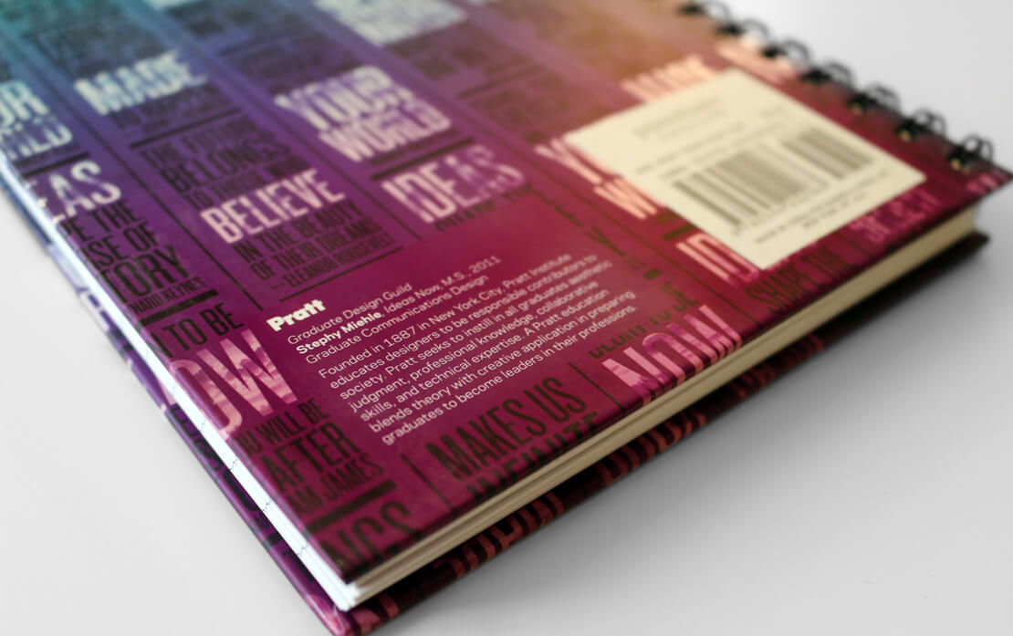 A vibrant spiral-bound notebook with a vibrant gradient from aqua to violet. The cover has multiple columns of inspirational quotes. The notebook is on a neutral surface with writing tools nearby.