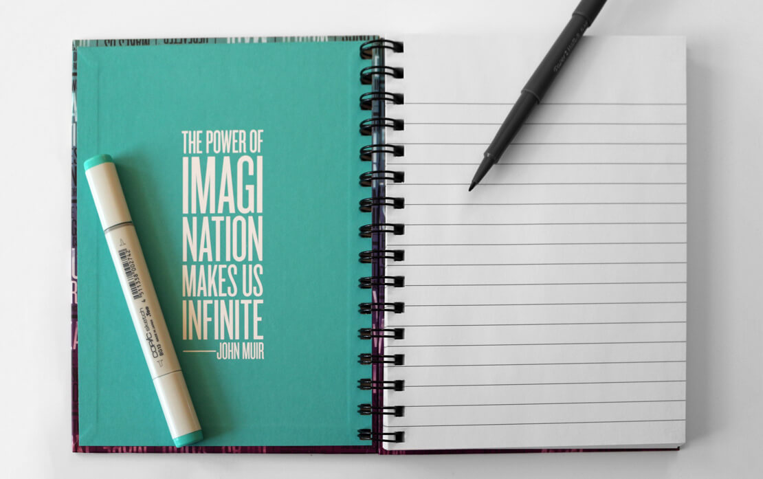 A vibrant spiral-bound notebook with a vibrant gradient from aqua to violet. The cover has multiple columns of inspirational quotes. The notebook is on a neutral surface with writing tools nearby.