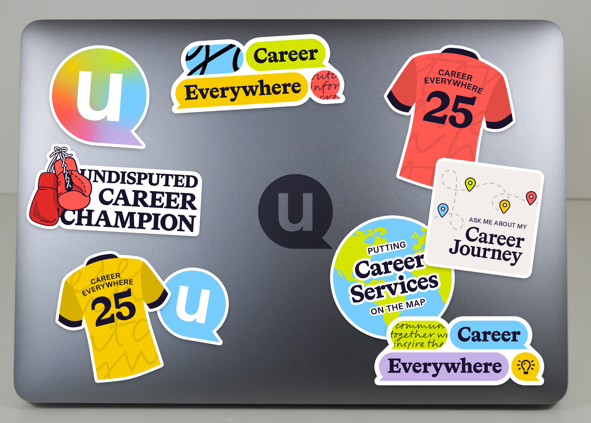 Various uConnect-themed stickers on a laptop. There are multiple colorways of a team jersey, 'Career Everywhere' banners with quote bubbles, a rainbow gradient 'u' logo, boxing gloves with 'Undisputed Career Champion' text, a doodled path with location pins and 'Ask me about my career journey' text, and a globe with text overlaid that says 'Putting career services on the map'.